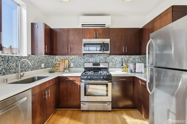 kitchen with sink, tasteful backsplash, a wall mounted AC, light wood-type flooring, and stainless steel appliances