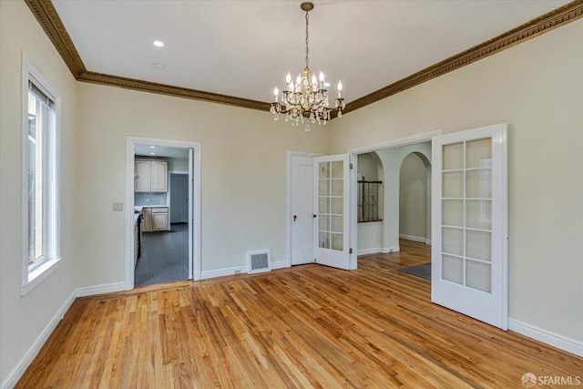 spare room featuring hardwood / wood-style flooring, ornamental molding, a chandelier, and french doors