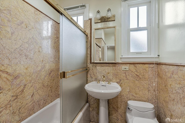 full bathroom with toilet, shower / bath combination with glass door, sink, and tile walls