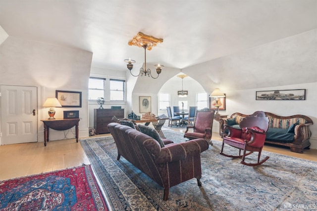 living room featuring arched walkways, a chandelier, wood finished floors, and vaulted ceiling