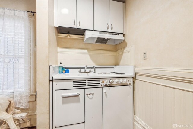 kitchen featuring white cabinets, cooktop, a wainscoted wall, under cabinet range hood, and light countertops