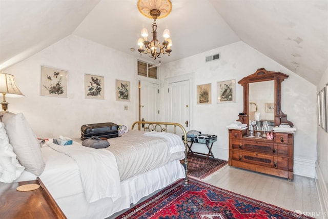bedroom featuring lofted ceiling, wood finished floors, visible vents, and a chandelier