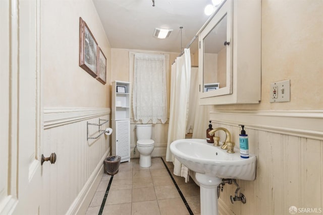 bathroom featuring toilet, wainscoting, visible vents, tile patterned flooring, and a shower with shower curtain