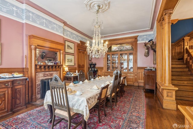 dining space with ornate columns, dark hardwood / wood-style floors, ornamental molding, a brick fireplace, and an inviting chandelier