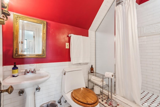 bathroom featuring a sink, toilet, tile walls, lofted ceiling, and a shower stall