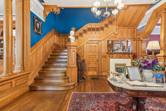 stairs with wooden walls, hardwood / wood-style floors, an inviting chandelier, and decorative columns