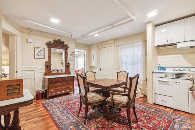 dining area featuring light wood-type flooring, a decorative wall, and a wainscoted wall
