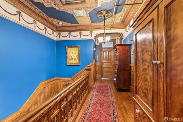 hall featuring an ornate ceiling, wood finished floors, wainscoting, a chandelier, and ornamental molding