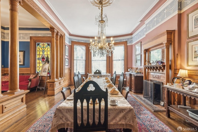 dining area featuring wainscoting, decorative columns, a notable chandelier, wood finished floors, and crown molding