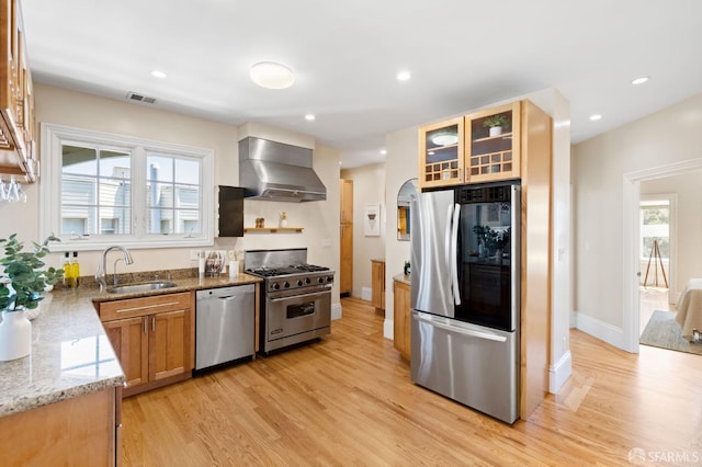 kitchen featuring sink, stainless steel appliances, light stone countertops, light hardwood / wood-style floors, and wall chimney range hood