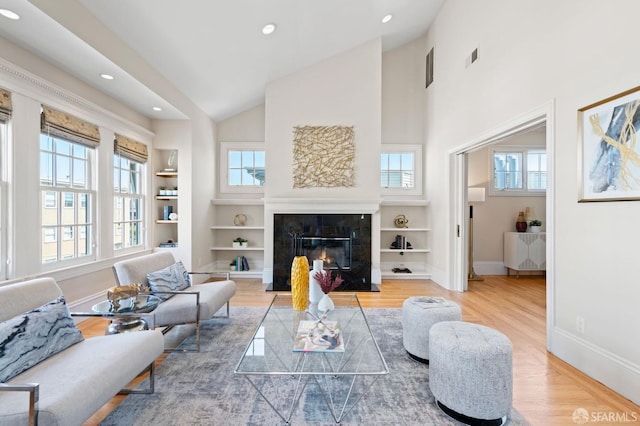 living room featuring a wealth of natural light, built in features, a premium fireplace, and wood-type flooring