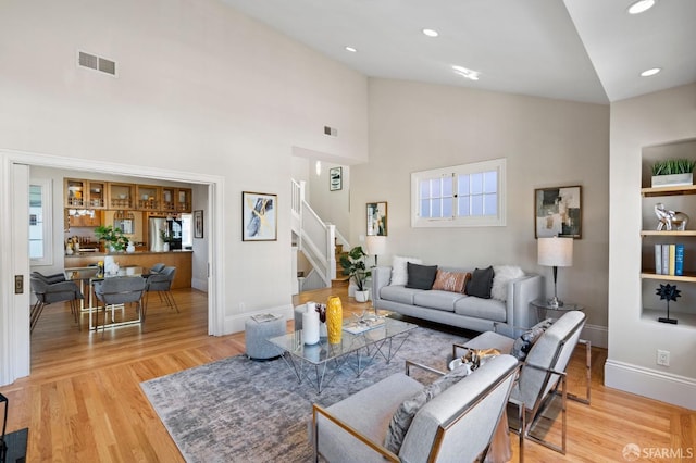 living room with high vaulted ceiling, light hardwood / wood-style floors, and built in features