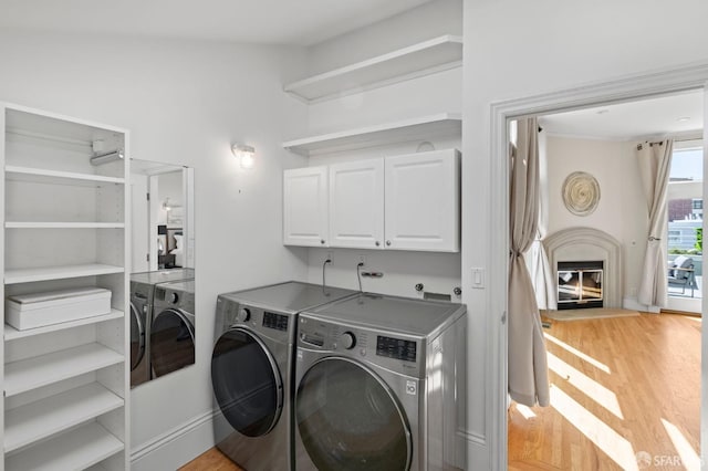 laundry room featuring cabinets, washing machine and dryer, and light hardwood / wood-style flooring