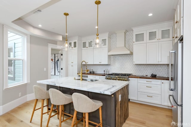 kitchen with stainless steel appliances, a center island with sink, sink, custom exhaust hood, and white cabinetry