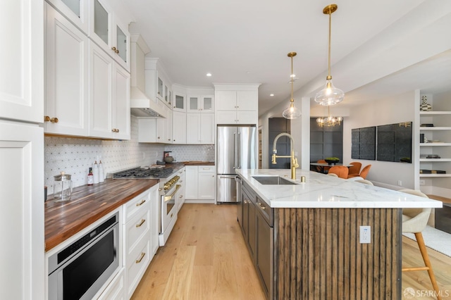 kitchen featuring appliances with stainless steel finishes, sink, light wood-type flooring, white cabinets, and a center island with sink