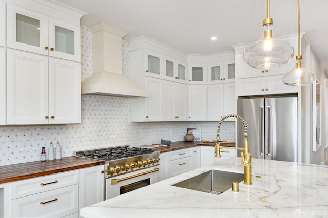 kitchen featuring sink, butcher block counters, hanging light fixtures, high end appliances, and premium range hood