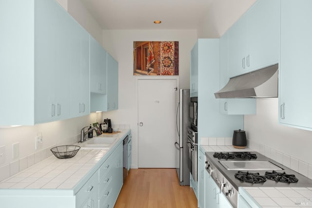 kitchen featuring sink, blue cabinetry, stainless steel appliances, light hardwood / wood-style floors, and tile countertops