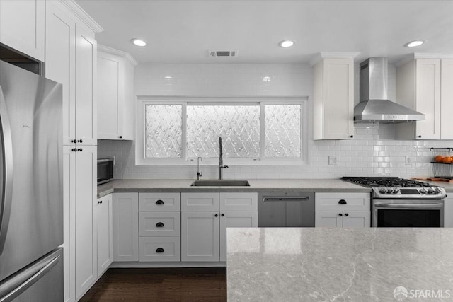 kitchen featuring wall chimney range hood, stainless steel appliances, sink, and white cabinets