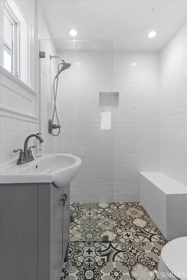 bathroom with tile walls, a tile shower, vanity, tile patterned floors, and toilet