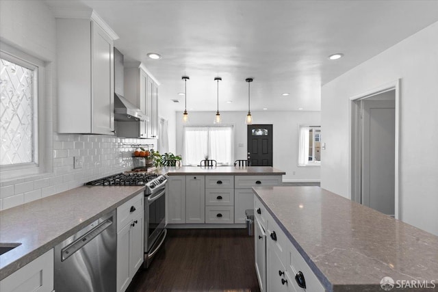 kitchen with appliances with stainless steel finishes, pendant lighting, white cabinetry, light stone countertops, and wall chimney exhaust hood