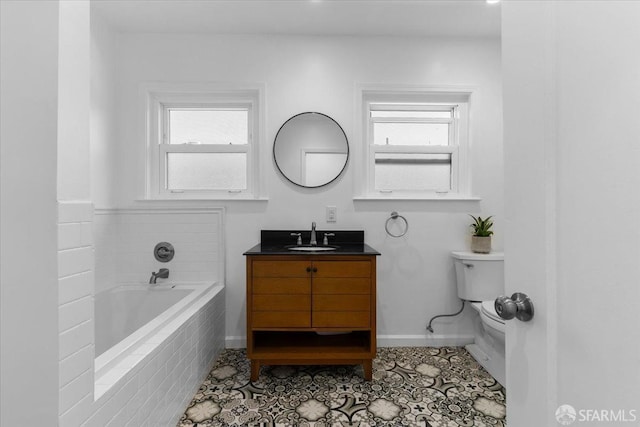 bathroom featuring vanity, a healthy amount of sunlight, tiled bath, and toilet