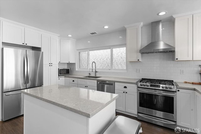 kitchen featuring wall chimney range hood, sink, appliances with stainless steel finishes, white cabinetry, and a center island