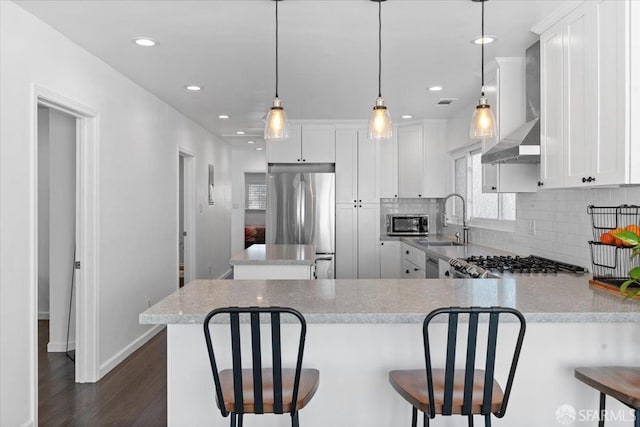 kitchen with sink, white cabinets, stainless steel fridge, hanging light fixtures, and wall chimney exhaust hood