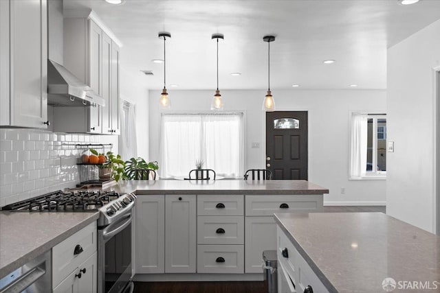 kitchen with wall chimney exhaust hood, tasteful backsplash, hanging light fixtures, appliances with stainless steel finishes, and white cabinets