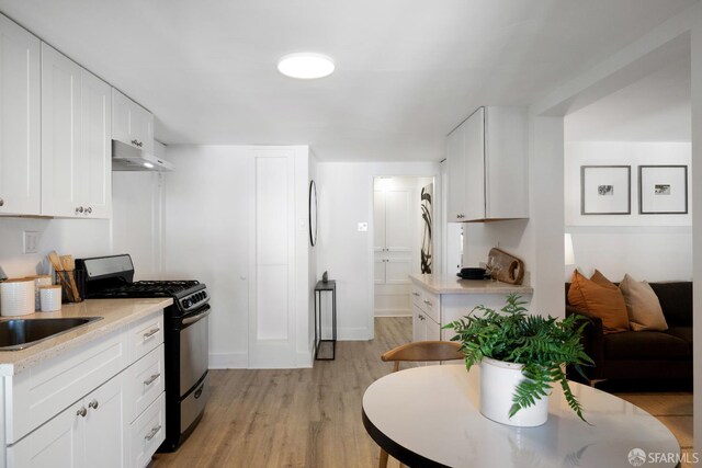 1141 Church St, San Francisco, CA 94114 - kitchen with stainless steel gas stove, under cabinet range hood, light countertops, light wood finished floors, and white cabinetry