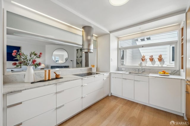 kitchen with light wood finished floors, a sink, black electric stovetop, white cabinetry, and modern cabinets