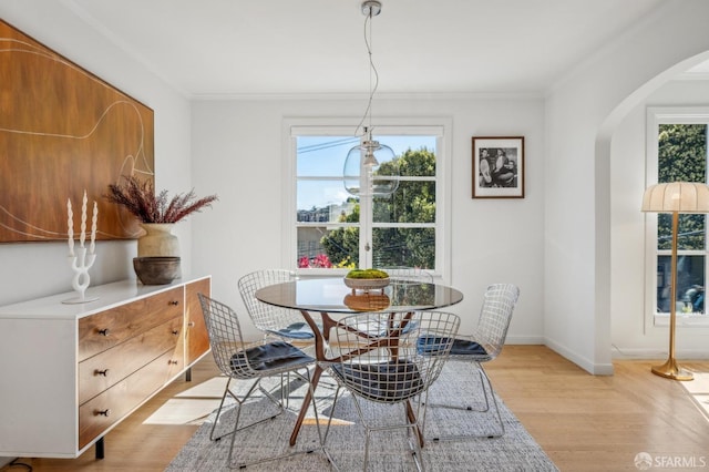 dining space with baseboards, arched walkways, light wood-style floors, and ornamental molding