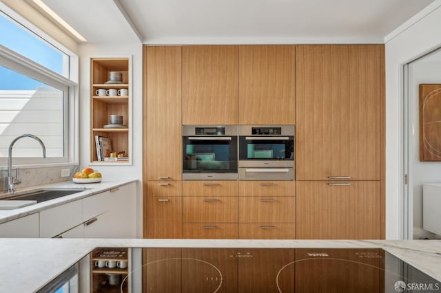 kitchen featuring a sink, modern cabinets, light stone counters, and a healthy amount of sunlight