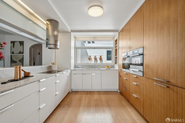 kitchen featuring oven, modern cabinets, white cabinetry, arched walkways, and light wood finished floors