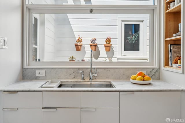 kitchen featuring white cabinetry, light stone counters, and a sink