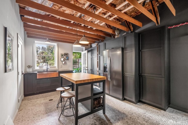 kitchen featuring wooden counters, beamed ceiling, pendant lighting, stainless steel fridge, and a sink