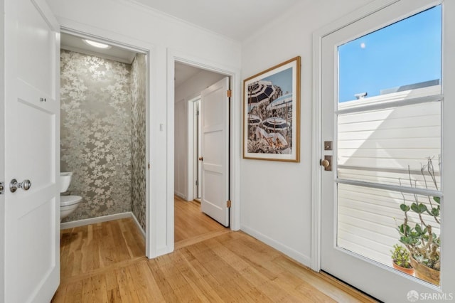 doorway to outside with baseboards, crown molding, and light wood finished floors