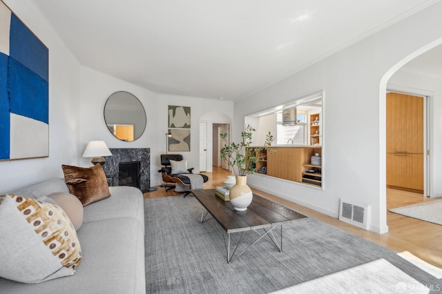 living room with visible vents, wood finished floors, arched walkways, a premium fireplace, and baseboards