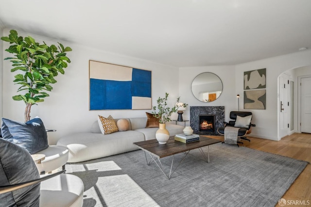 living area with wood finished floors, arched walkways, a high end fireplace, and baseboards