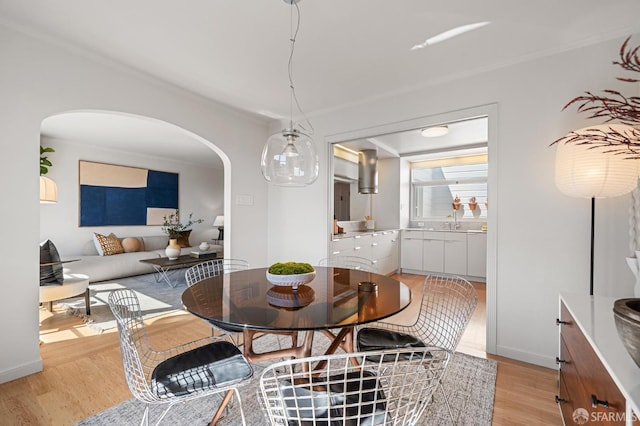 dining space with light wood-type flooring, arched walkways, baseboards, and ornamental molding