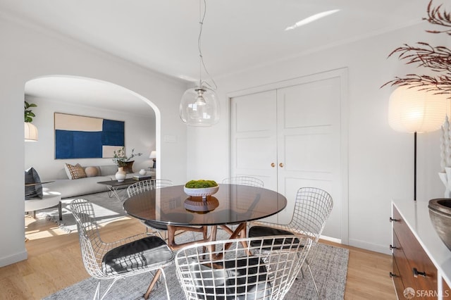 dining area with arched walkways, baseboards, and light wood-style floors