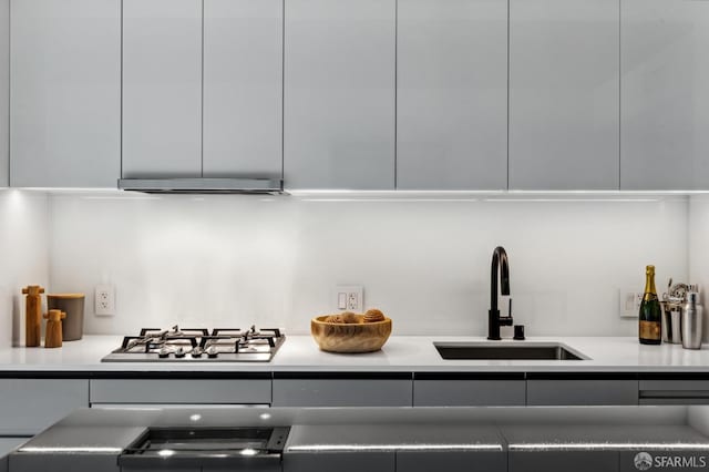 kitchen with stainless steel gas cooktop, modern cabinets, a sink, and under cabinet range hood