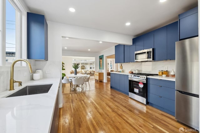 kitchen with sink, blue cabinetry, appliances with stainless steel finishes, and light wood-type flooring