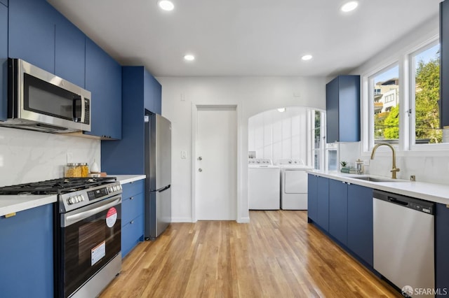 kitchen featuring appliances with stainless steel finishes, independent washer and dryer, blue cabinets, light hardwood / wood-style floors, and sink