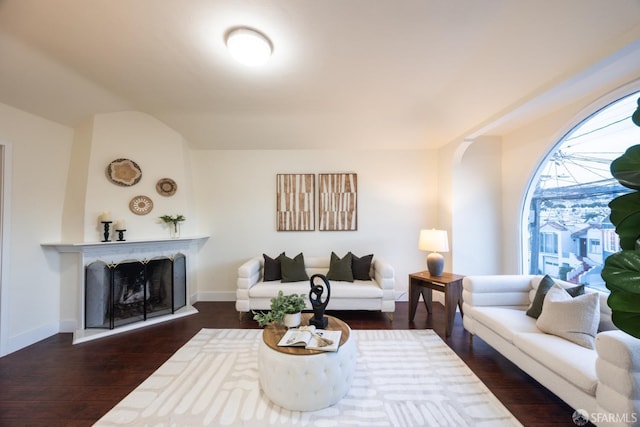 living area with a fireplace with raised hearth, dark wood-type flooring, lofted ceiling, and baseboards