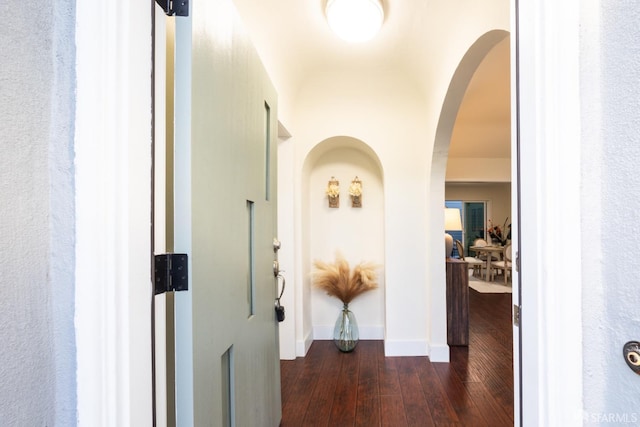 corridor featuring dark wood-style floors, arched walkways, and baseboards