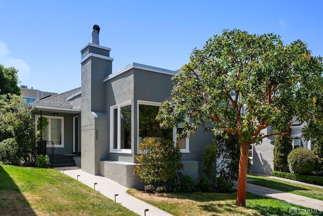 view of front of house with stucco siding, a front lawn, and a chimney