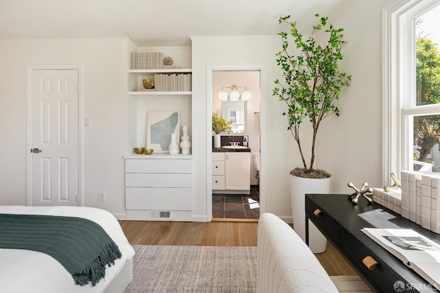 bedroom with wood finished floors, ensuite bathroom, and a chandelier