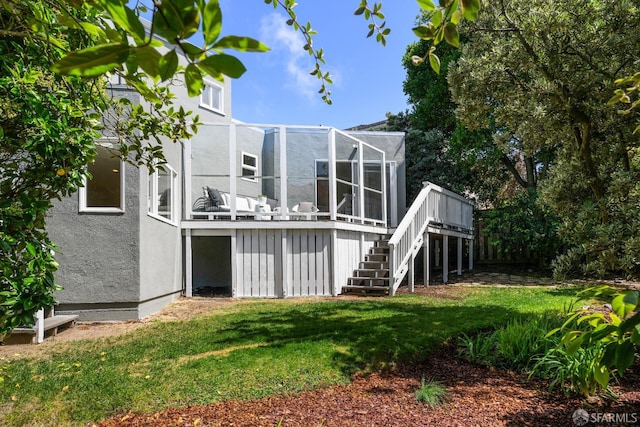 back of property featuring stairway, stucco siding, a deck, a yard, and a lanai