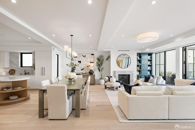 living area with recessed lighting, an inviting chandelier, light wood-style flooring, and a high end fireplace