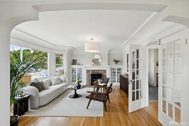 living area with ornamental molding, arched walkways, wood finished floors, and a tile fireplace